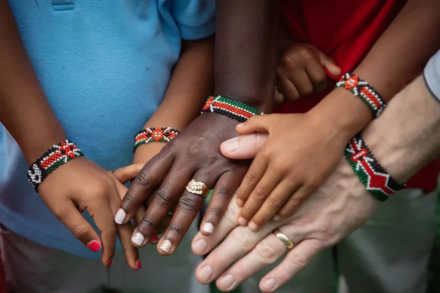 Children's wrists side by side, wearing beaded bracelets in the colours of the Kenyan flag.
